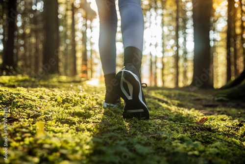 Sporty woman running in the forest at sunrise. Close up of sport shoes. Fitness and workout wellness concept.