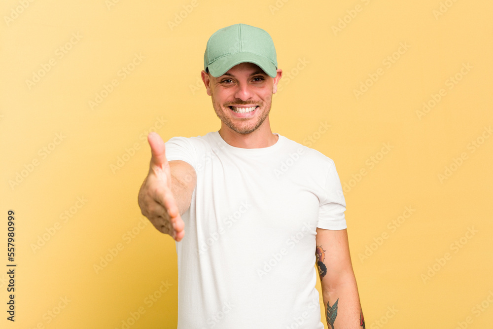 Young caucasian handsome man isolated on yellow background stretching hand at camera in greeting gesture. Young caucasian handsome man isolated on yellow background stretching hand at camera in greeting gesture.
