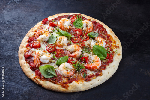 Traditionelle italienische Pizza frutti di mare Riesengarnelen, Tomaten und Mozzarella serviert als close-up auf einem rustikalen schwarzen Board 