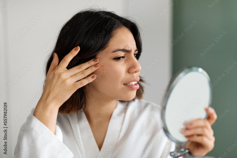 Sad young woman suffering from acne, checking skin in mirror Sad young woman suffering from acne, checking skin in mirror