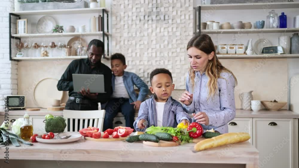 Pretty mother and son preparing tasty food at kitchen. Mommy teaching lovely kid to cook while happy father and child boy spending time using laptop computer. Healthy meal and dinner preparation. Pretty mother and son preparing tasty food at kitchen. Mommy teaching lovely kid to cook while happy father and child boy spending time using laptop computer. Healthy meal and dinner preparation.