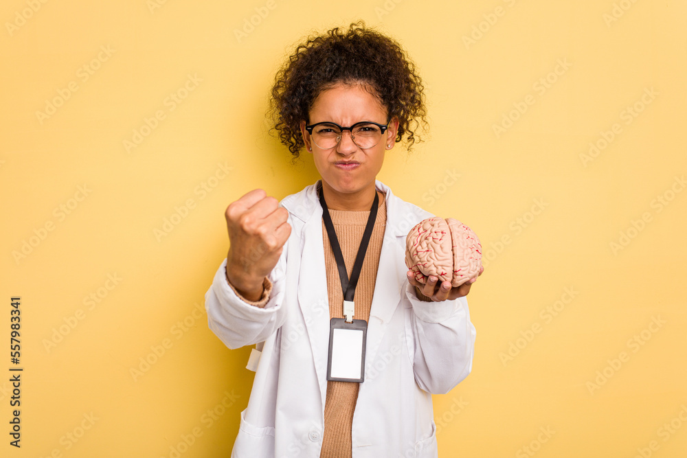 Young doctor brazilian woman holding a brain model isolated showing fist to camera, aggressive facial expression. Young doctor brazilian woman holding a brain model isolated showing fist to camera, aggressive facial expression.