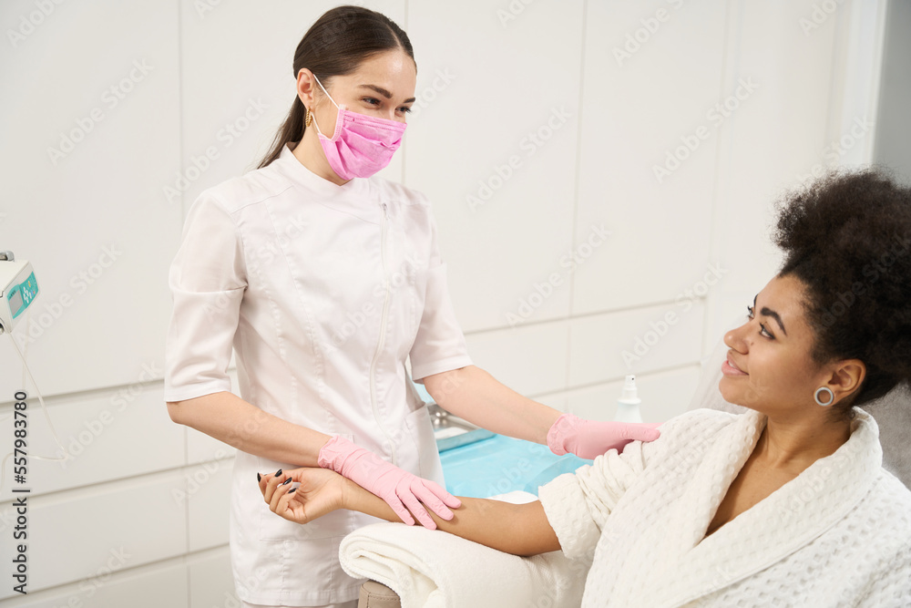 Smiling cosmetologist talking with patient before procedure in private clinic Smiling cosmetologist talking with patient before procedure in private clinic