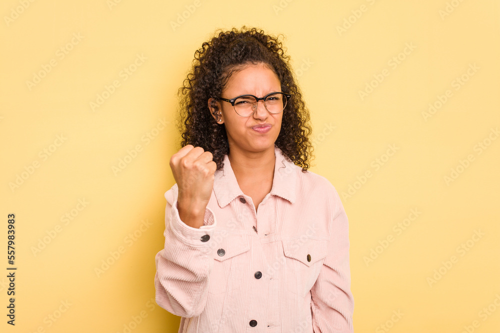 Young Brazilian curly hair cute woman isolated on yellow background showing fist to camera, aggressive facial expression. Young Brazilian curly hair cute woman isolated on yellow background showing fist to camera, aggressive facial expression.