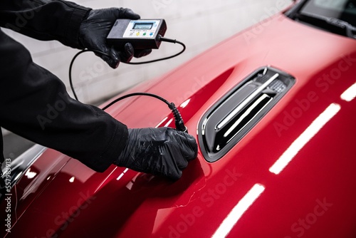 Canvas Print Employee of a car service checks the thickness of the paint coating of a red car
