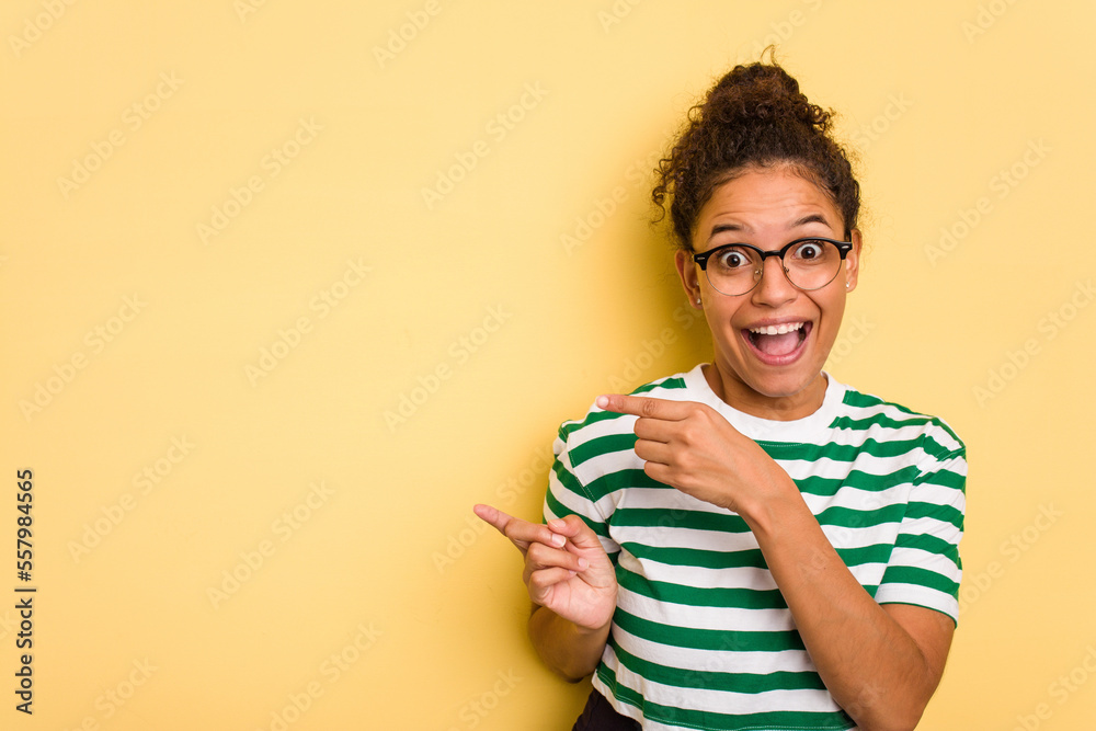Young Brazilian curly hair cute woman isolated on yellow background excited pointing with forefingers away.
