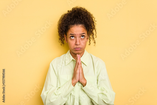 Young Brazilian curly hair cute woman isolated on yellow background holding hands in pray near mouth, feels confident.