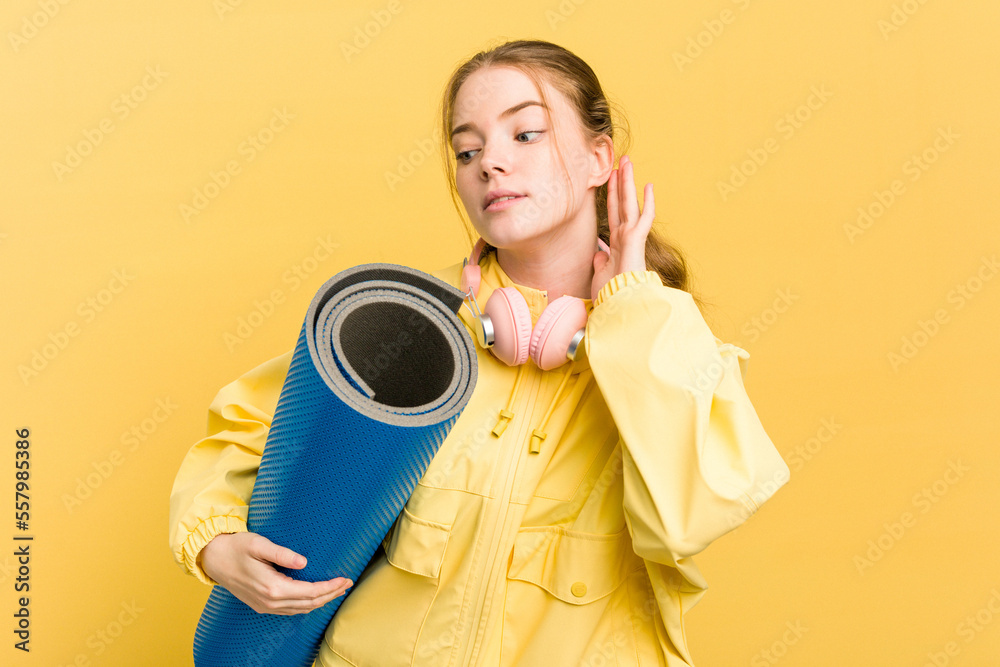 Young sport woman going to yoga classes while she is holding a mat isolated on yellow background trying to listening a gossip. Young sport woman going to yoga classes while she is holding a mat isolated on yellow background trying to listening a gossip.