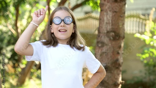 Young happy curious elementary school age girl, clever intelligent genius child student in big funny glasses has a brilliant idea, finger pointing up, eureka pose concept one person, outdoors portrait