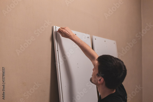 A young man is screwing a screw into a board with his hands.