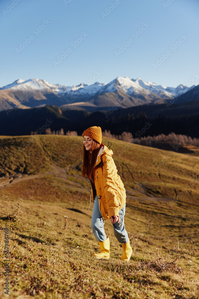 Full-length woman running up the hill to the camera and looking out at the mountains in a yellow raincoat and jeans in the autumn happy sunset camping trip, freedom lifestyle 