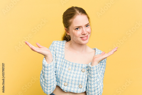 Young caucasian redhead woman isolated on yellow background doubting and shrugging shoulders in questioning gesture.