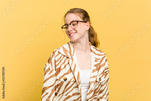 Young caucasian redhead woman isolated on yellow background looks aside smiling, cheerful and pleasant.