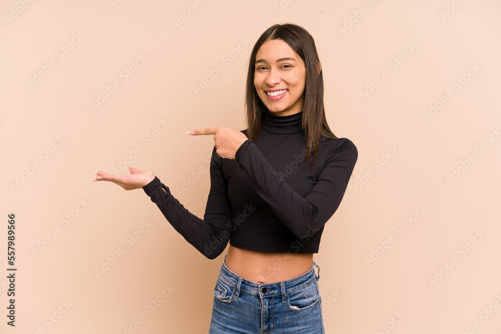 Young colombian woman isolated on beige background excited holding a copy space on palm. Young colombian woman isolated on beige background excited holding a copy space on palm.