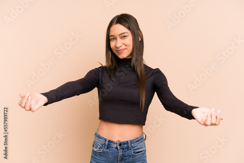 Young colombian woman isolated on beige background showing a welcome expression.