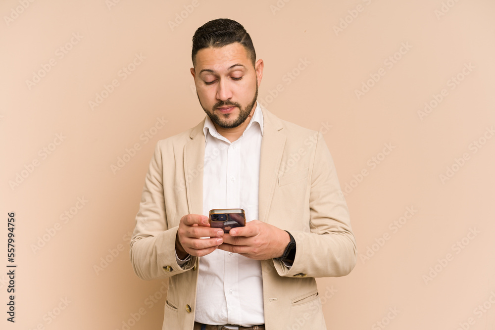 Adult latin business man using mobile phone isolated on beige background Adult latin business man using mobile phone isolated on beige background