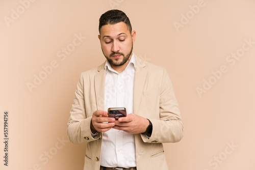 Adult latin business man using mobile phone isolated on beige background © Asier