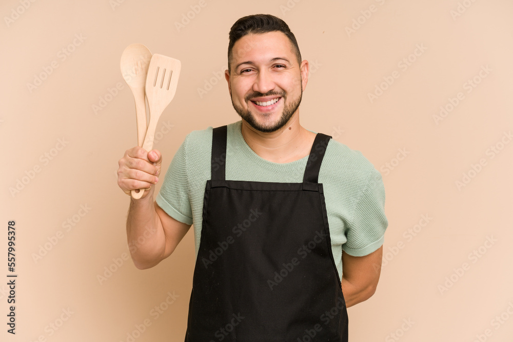 Adult latin cook man holding wooden utensils isolated Adult latin cook man holding wooden utensils isolated