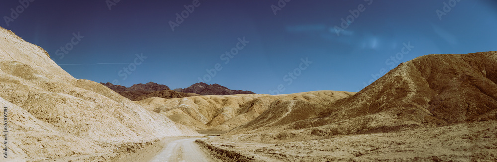 Unpaved sandy road between desert colorful mountains in Death Valley at sunny day