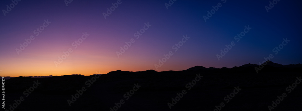 Panorama shot of dark blue and violet sky with remnants of orange sunset and black silhouette of horizon