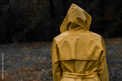 Mysterious woman covered by yellow coat while raining. The figure has his back with his face covered and looks towards the dark forest. Selective color. photo