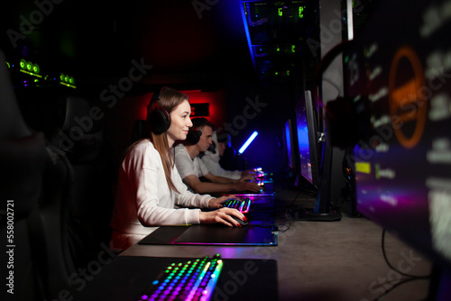 Photography girl gamer sits in headphones in a computer club and plays a game with a team