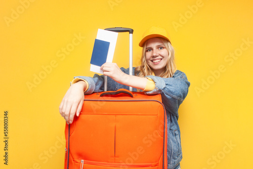 happy girl tourist with a suitcase and tickets smiling on yellow isolated background, travel concept