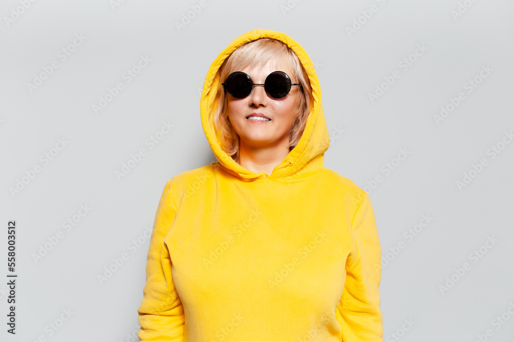Portrait of a smiling blonde woman, wearing yellow hoodie, wearing black sunglasses. Portrait of a smiling blonde woman, wearing yellow hoodie, wearing black sunglasses.