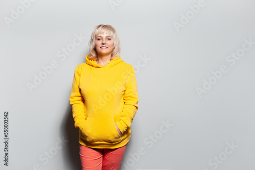 Portrait of a smiling blonde woman, wearing yellow hoodie and pink pants.