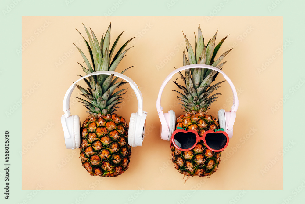 Two pineapples in sunglasses with headphones on light green and yellow background. Summer concept. Top view, flat lay