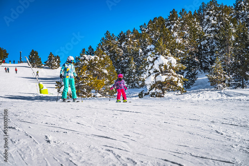 Mother and daughter skiing down a slope on a winter ski holidays in Andorra, El Tarter Snowy forest in Pyrenees Mountains