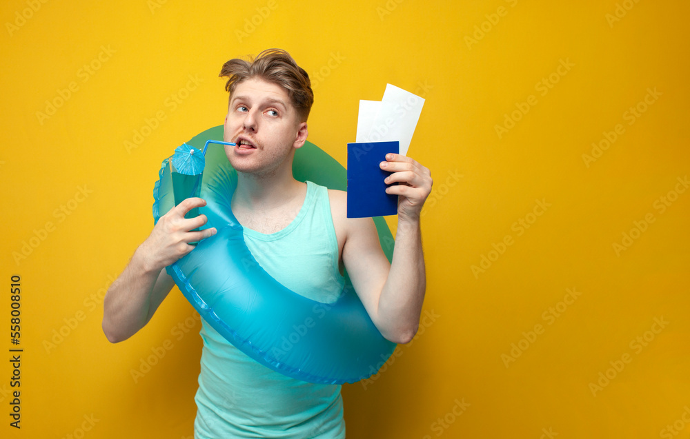 young guy in the summer on vacation with an inflatable swimming circle shows a passport and drinks a cocktail young guy in the summer on vacation with an inflatable swimming circle shows a passport and drinks a cocktail