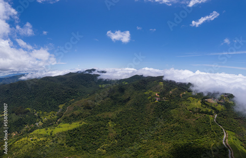 Aerial image of mountains with low clouds covering part of the landscape. Heavy clouds  green vegetation and very blue sky. Mist and white clouds.