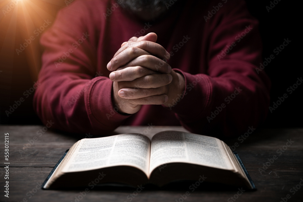 Hands folded in prayer on a Holy Bible in church concept for faith, spirituality and religion, man praying in morning. Man hand with Bible praying. Person Christian who faith in Jesus worship in dark. Hands folded in prayer on a Holy Bible in church concept for faith, spirituality and religion, man praying in morning. Man hand with Bible praying. Person Christian who faith in Jesus worship in dark.