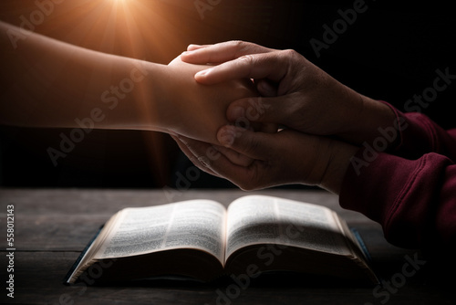 Hands folded in prayer on a Holy Bible in church concept for faith, spirituality and religion, man praying in morning. Man hand with Bible praying. Person Christian who faith in Jesus worship in dark. © doidam10