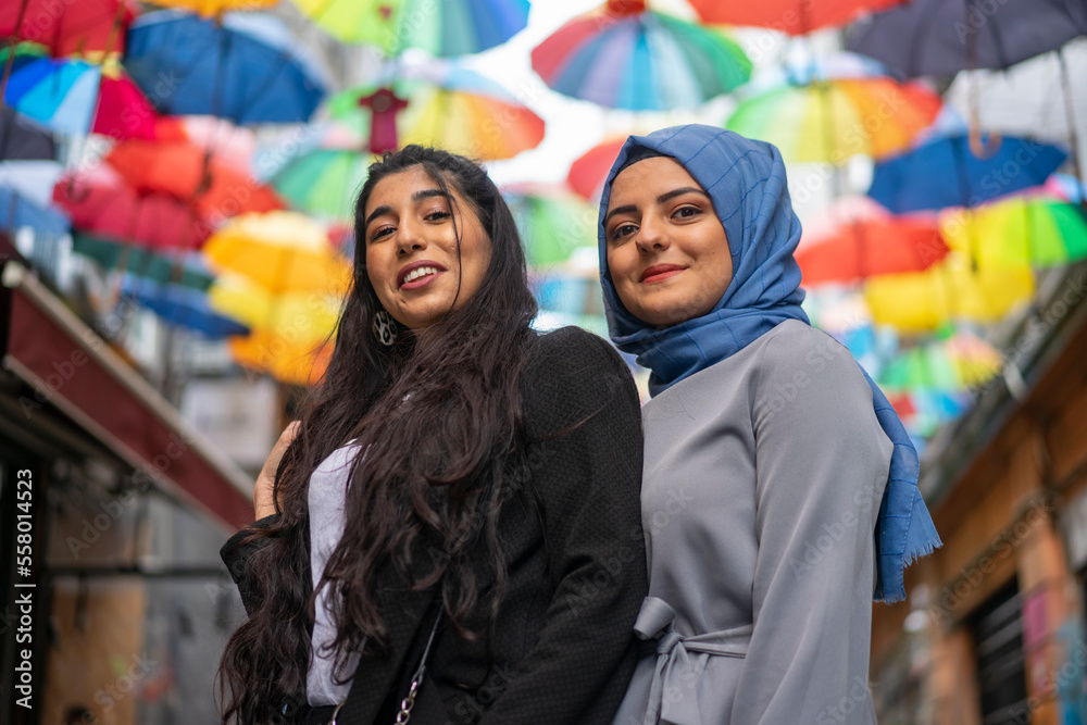 two woman hugging - with hijab and without. Colorful umbrella