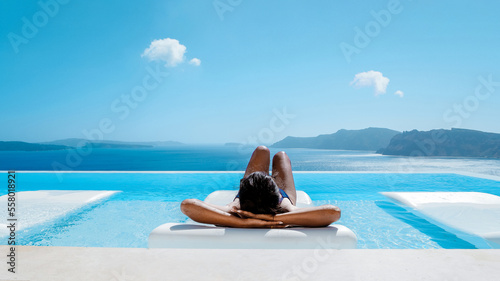 Schilderij op canvas Young multicultural Asian woman in the Infinity swimming pool looking out over the ocean caldera of Oia Santorini Greece