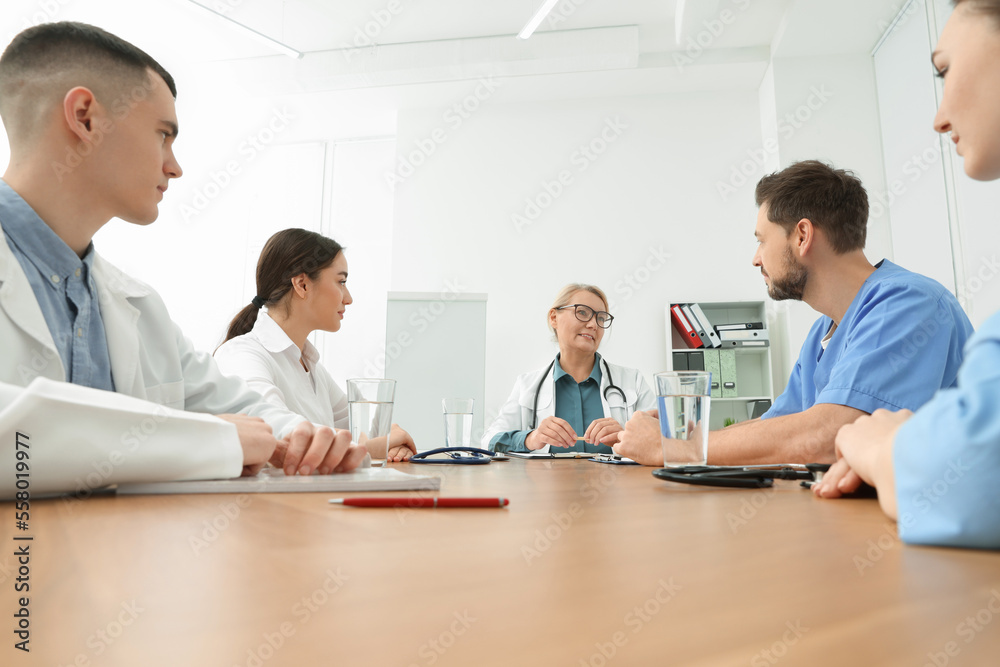 Medical conference. Team of doctors having discussion with speaker at wooden table in clinic Medical conference. Team of doctors having discussion with speaker at wooden table in clinic