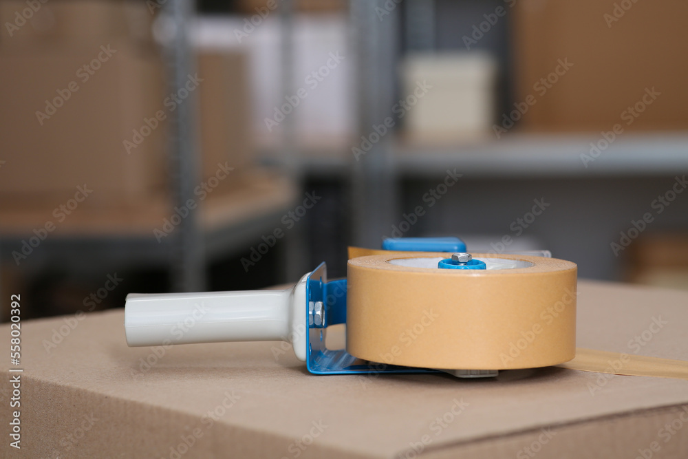 Adhesive tape dispenser on cardboard box indoors, closeup