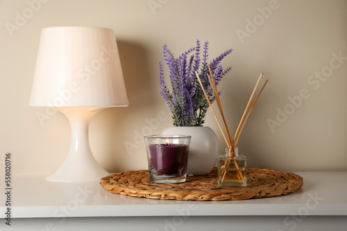 Aromatic reed air freshener, candle, lamp and lavender flowers on white table indoors