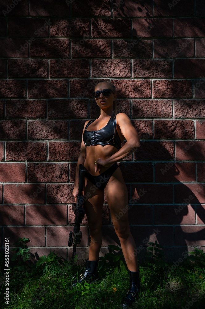 A caucasian woman in a bikini holds a machine gun against a brick wall. A caucasian woman in a bikini holds a machine gun against a brick wall.