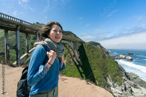 smiling asian Taiwanese female visitor enjoying amazing coastal view with big sur bridge at background under blue sky