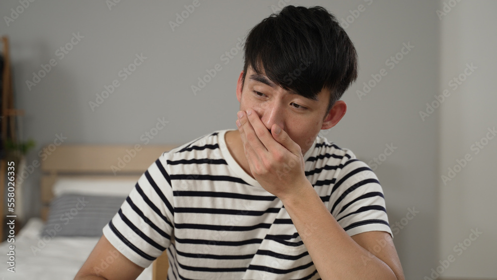 sleepy japanese adult student learning from home is holding head and looking at the webcam with a yawn while taking a boring online class in the bedroom. sleepy japanese adult student learning from home is holding head and looking at the webcam with a yawn while taking a boring online class in the bedroom.