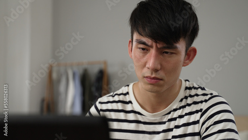 overworked Japanese young student having sudden blurry vision is rubbing his eyes while working from home on the computer.