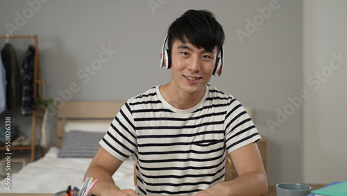 asian college Japanese boy learning from home with a headset is looking at camera and talking with ok hand gesture during a virtual online course in the bedroom at home