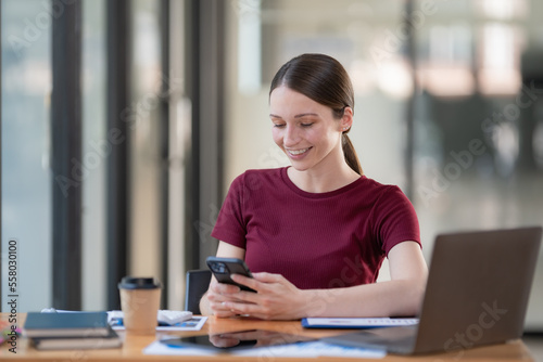 An attractive businesswoman sitting at her desk, holding a smartphone, smiling