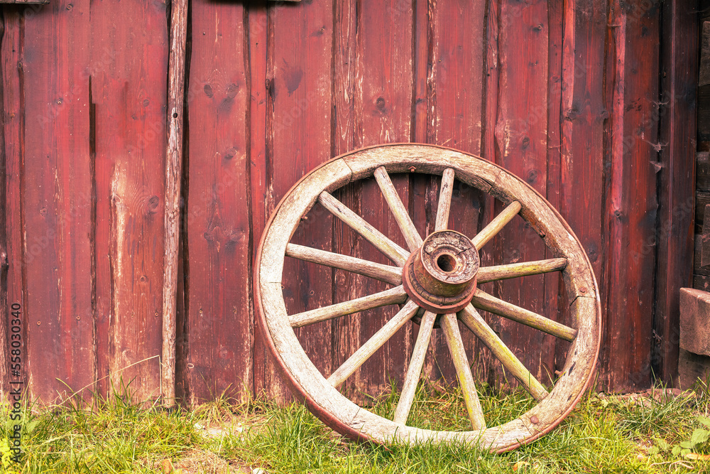 Old rusty wagon wheel leans against barn.Peasant tool. Old rusty wagon wheel leans against barn.Peasant tool.