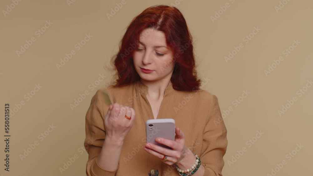 Sincere redhead woman customer using credit bank card and smartphone while transferring money, purchases online shopping, payment. Finance and internet. Young girl isolated alone on beige background Sincere redhead woman customer using credit bank card and smartphone while transferring money, purchases online shopping, payment. Finance and internet. Young girl isolated alone on beige background