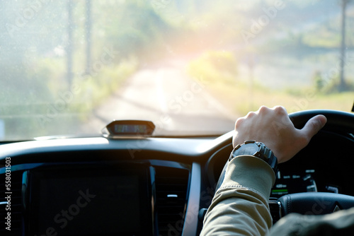 Man sit in the car hand is driving the car on the road. travel to He is looking to a road traffic route and listening to music happily 