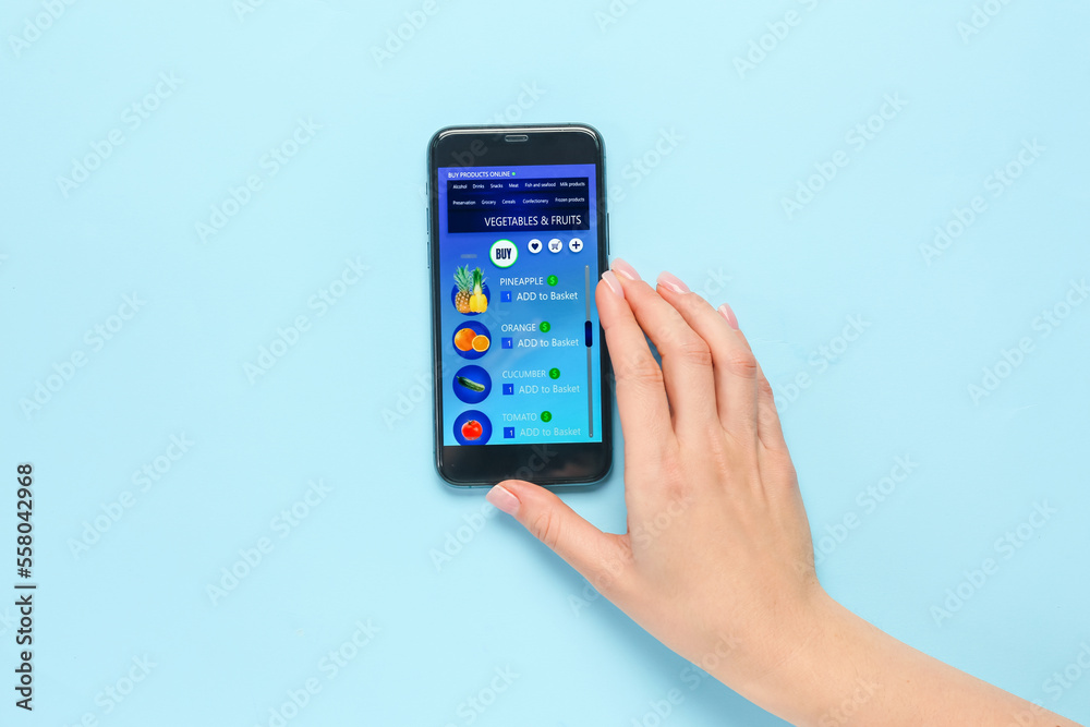 Woman using mobile phone with opened page of online grocery shop on color background Woman using mobile phone with opened page of online grocery shop on color background